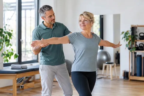 Physiotherapeut begleitet eine erwachsene Patientin bei einer Bewegungsübung in einer Praxis.