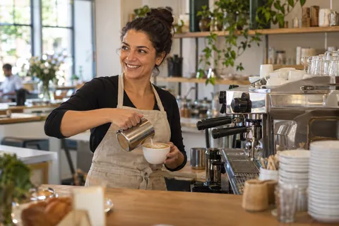 Barista bereitet einen Cappuccino an der Espressomaschine eines hellen Cafés zu.